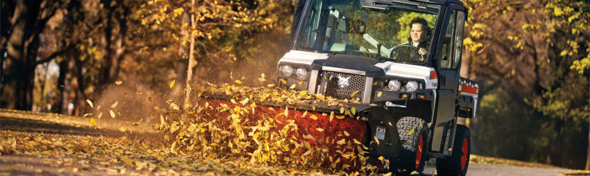 Man riding a Bobcat® 3650 UTV with an attachment cleaning leaves off a street.