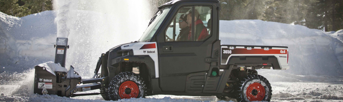 Orange & white Bobcat® 3650 UTV with a snowblower attachment in action moving through the snow